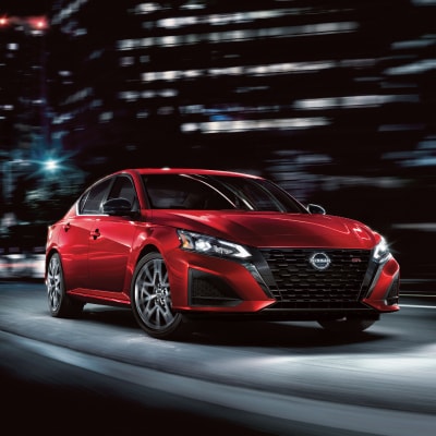 Angled front view of a red 2024 Nissan Altima driving fast down a dark city street