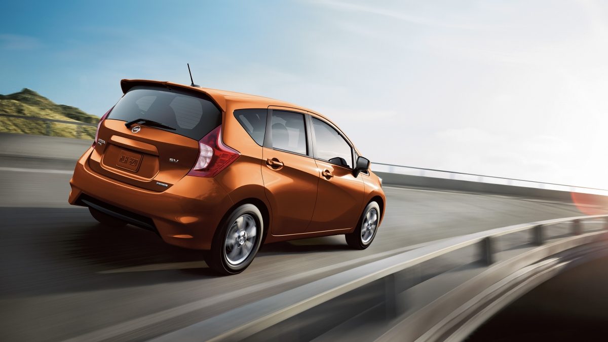 A rear view of a Nissan Versa Note SV in orange driving on a highway through mountains