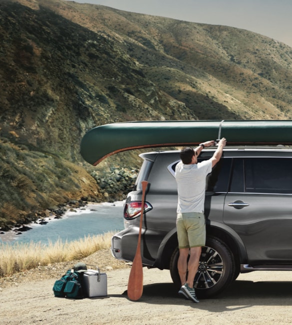 A man strapping a canoe to the top of a Nissan Armada SUV