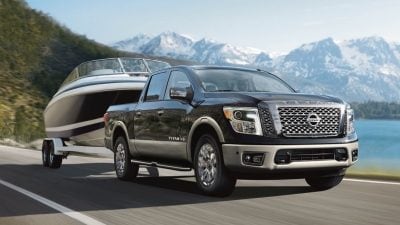 A Black 2020 Nissan Titan pickup with gray trim towing a boat on a mountain highway