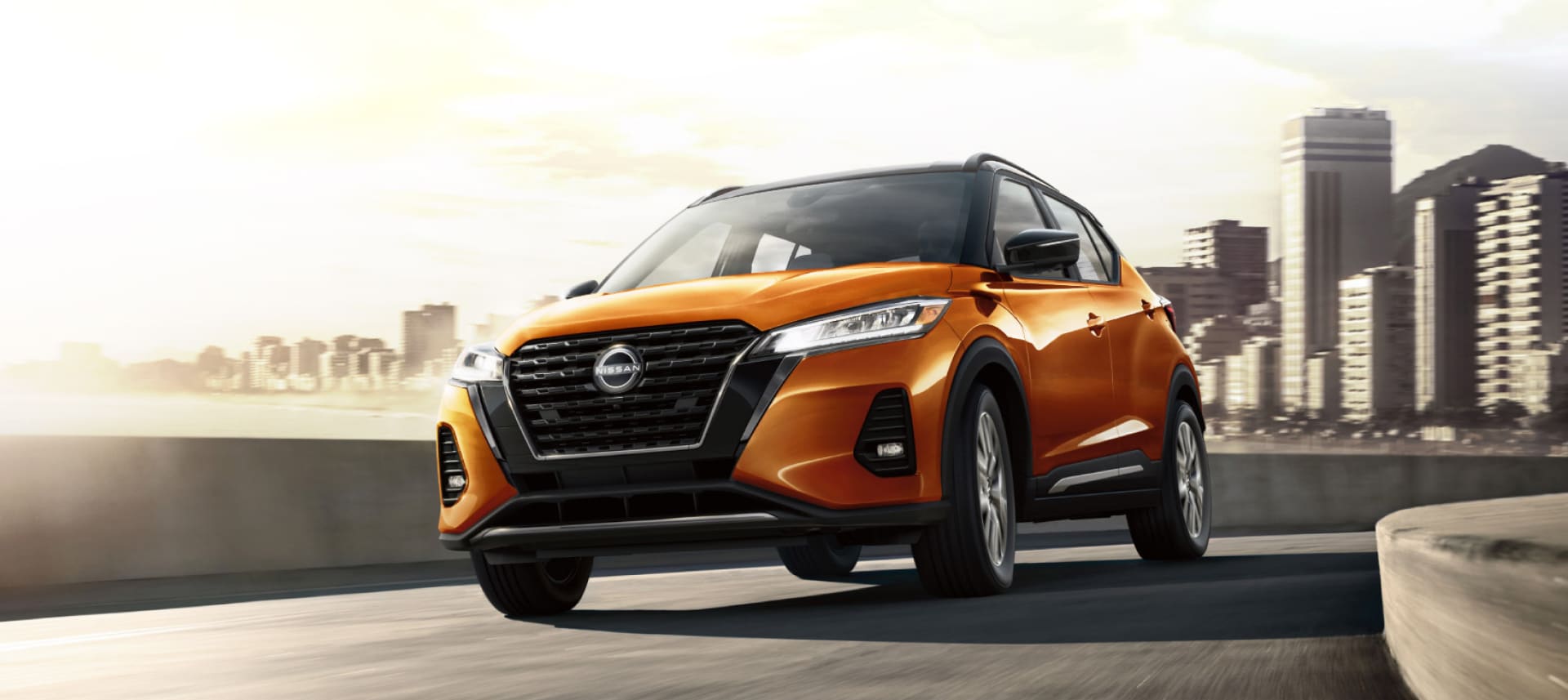 2024 Nissan Kicks in orange on a highway with city in background